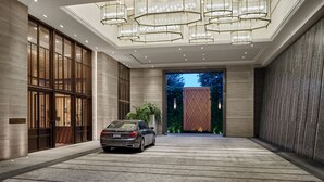 Eine geräumige, gut beleuchtete Lobby mit einem modernen Kronleuchter, einem BMW davor und Blick auf Grünflächen.