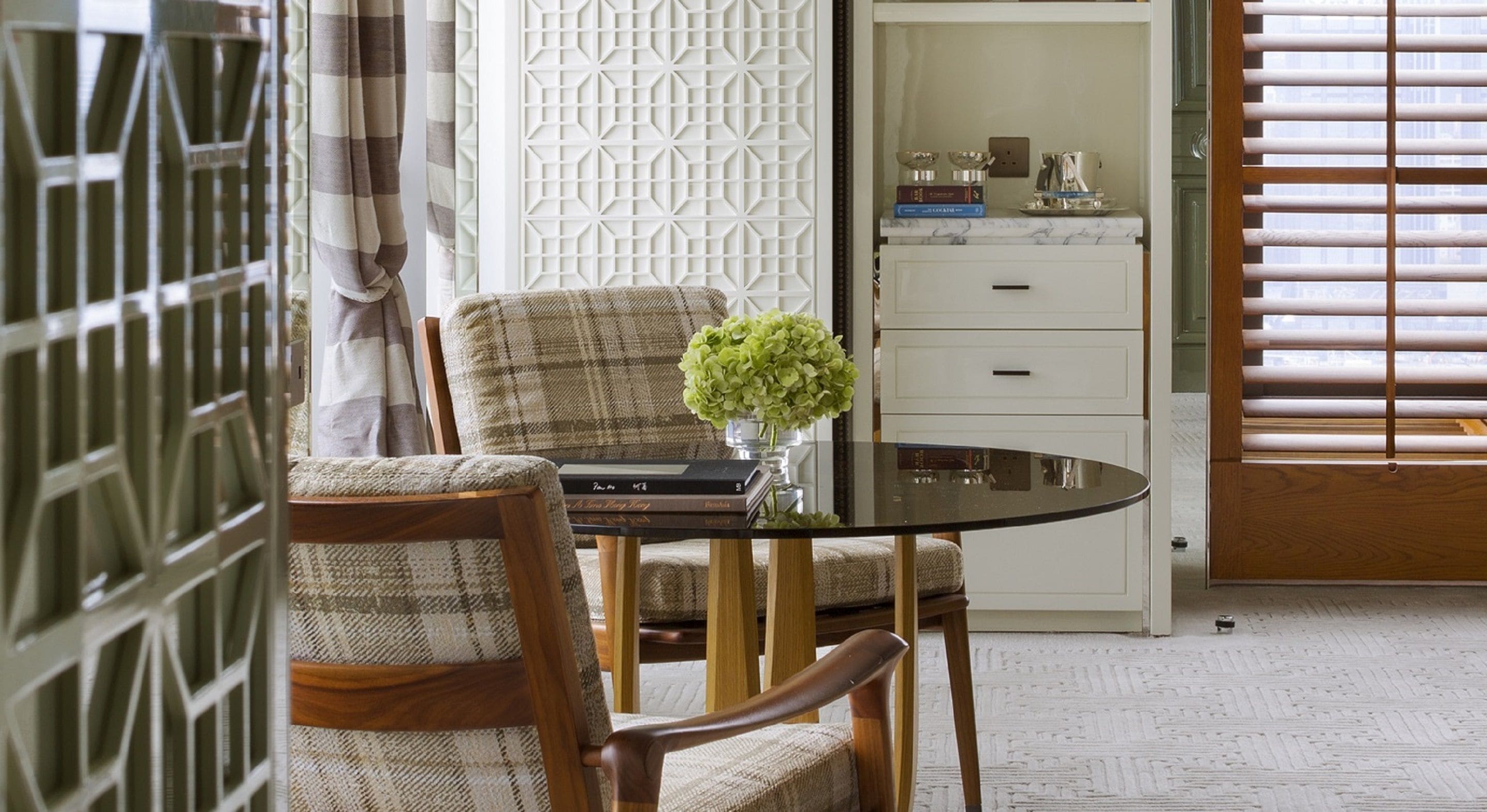 A dining area with a round table, two chairs, a vase with flowers, and a cabinet with books and decorative items.