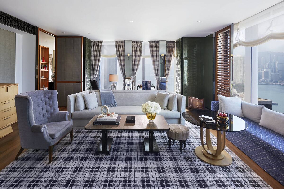 A modern living room with a sofa, armchairs, a coffee table, and a view of a cityscape through large windows.