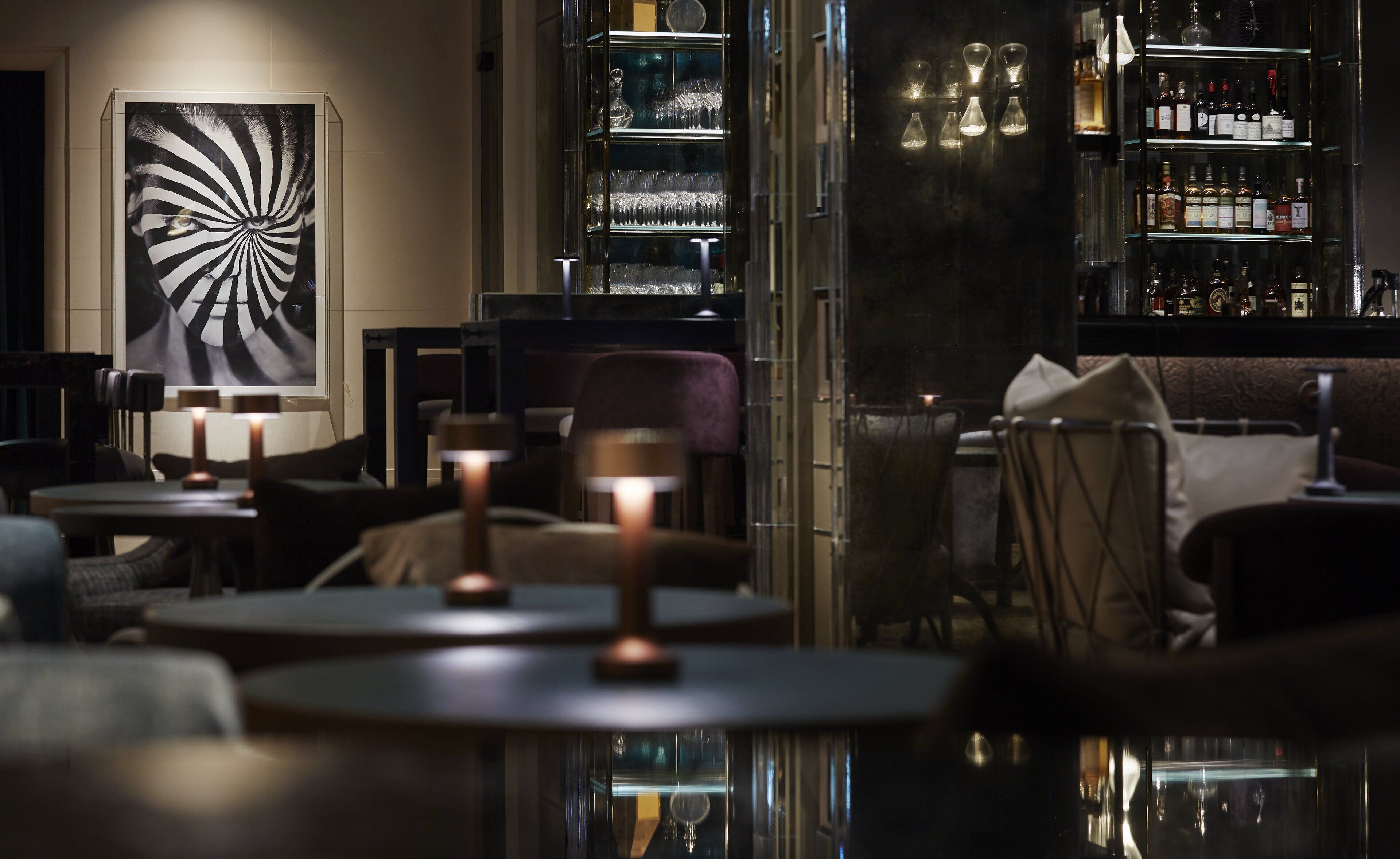 A dimly lit bar area with tables, chairs, and a large abstract painting on the wall.