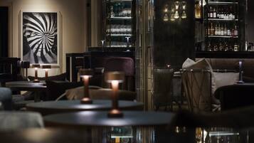 A dimly lit bar area with tables, chairs, and a large abstract painting on the wall.