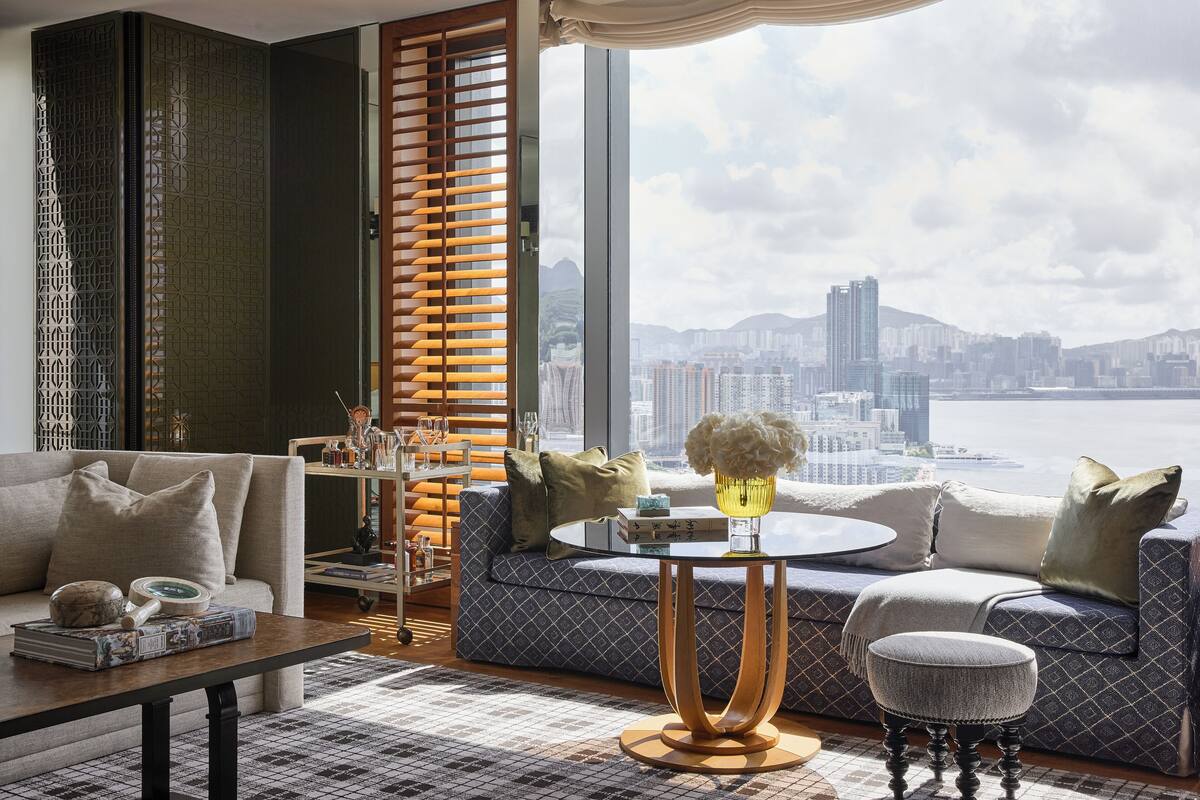 A modern living room with a sofa, coffee table, and ottoman, featuring a city view through large windows.