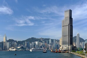 A city skyline with modern skyscrapers, a cruise ship docked at a harbor, and a mountainous backdrop. - Rosewood Hong Kong (Kowloon)