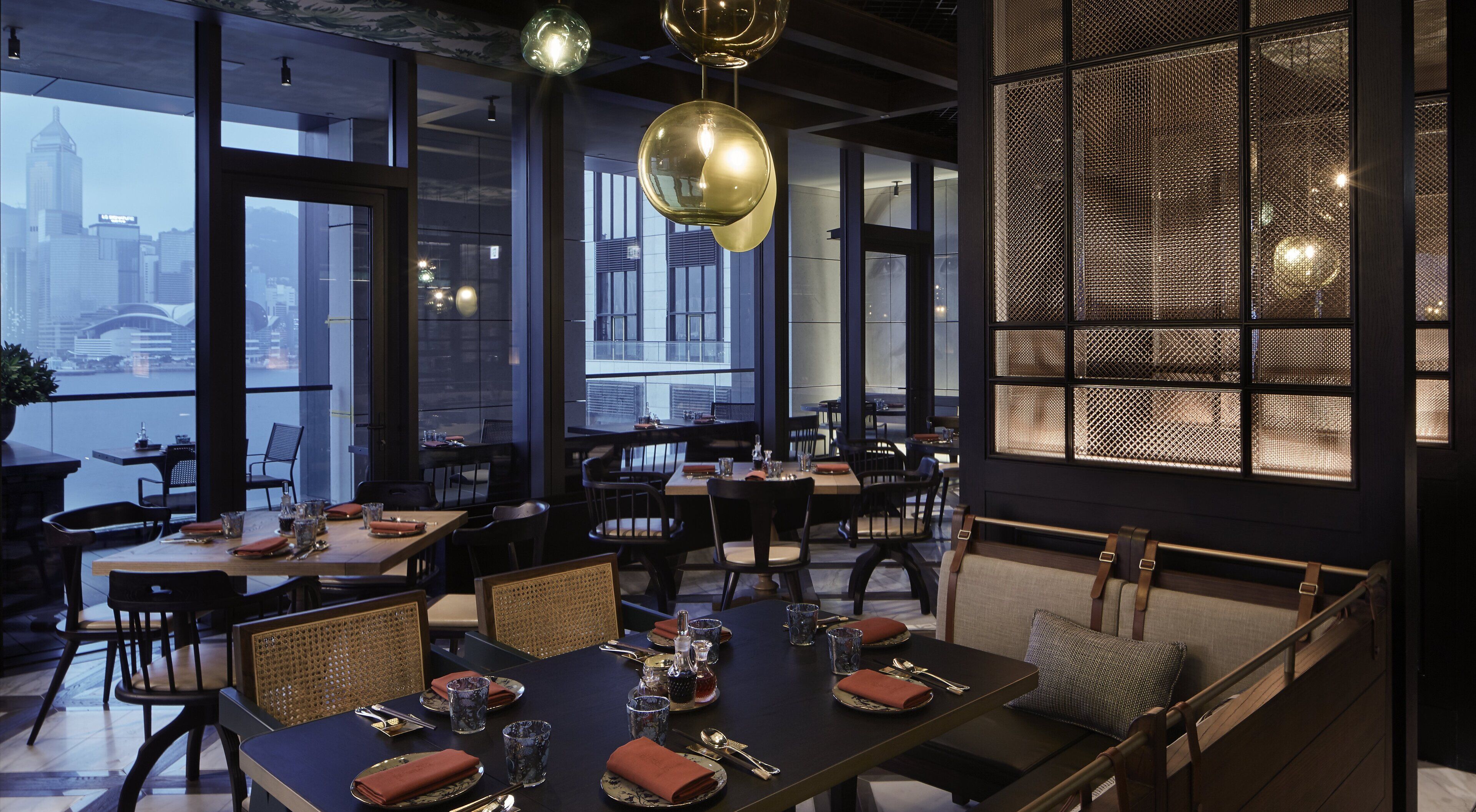 A modern restaurant with large windows, a city view, and a mix of seating arrangements.