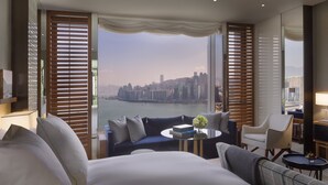 A hotel room with a large bed, a sofa, a coffee table, and a view of a cityscape and river.