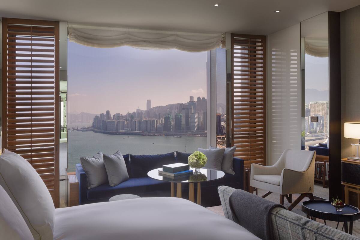 A hotel room with a large bed, a sofa, a coffee table, and a view of a cityscape and river.