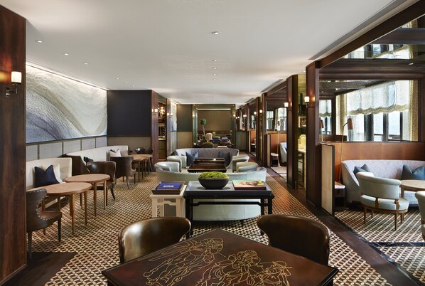 A modern hotel lobby with a geometric patterned floor, comfortable seating areas, and large windows providing natural light. - Rosewood Hong Kong (Kowloon)