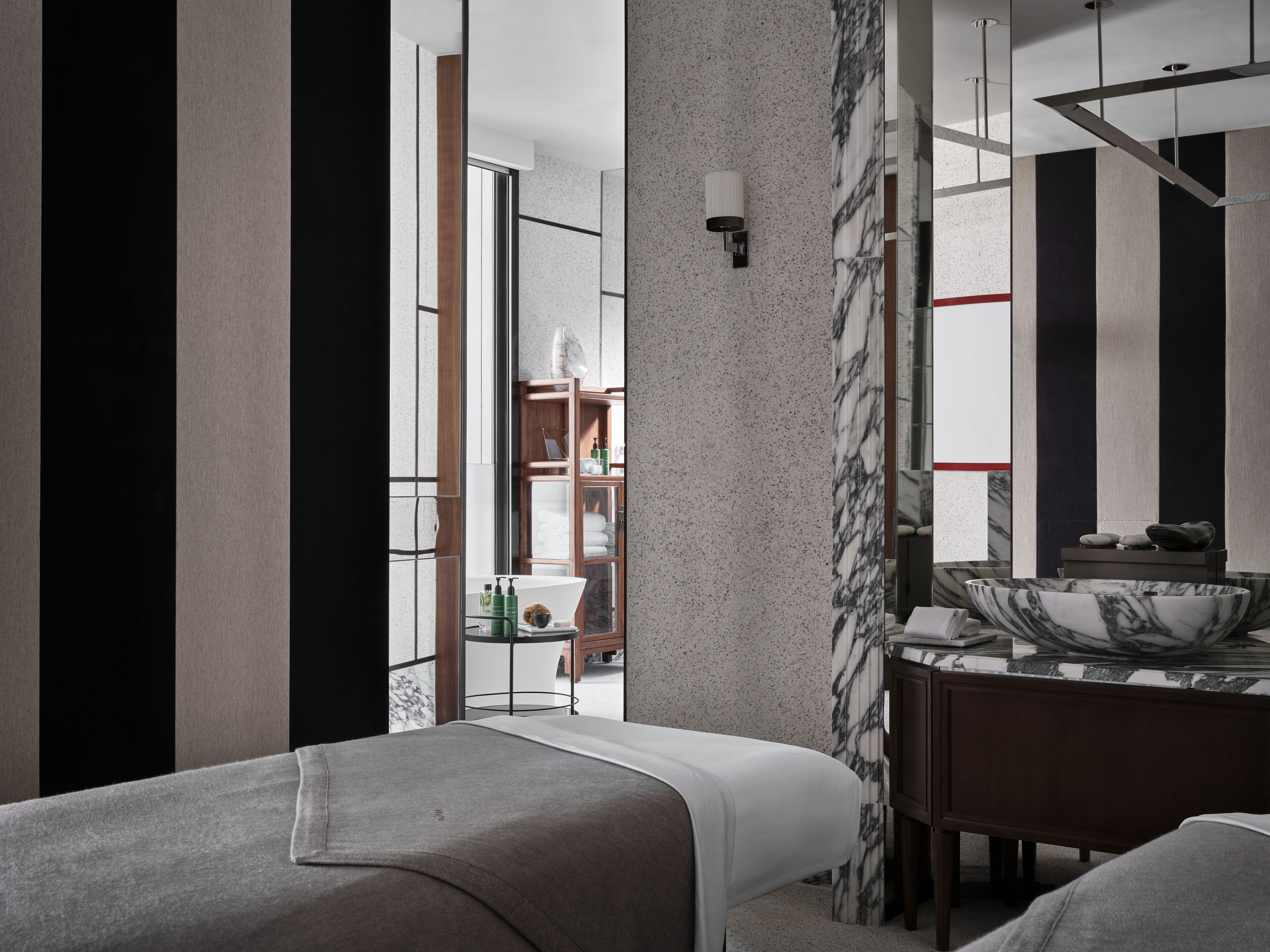 A modern hotel room with a large mirror, a marble column, and a wooden cabinet with toiletries.