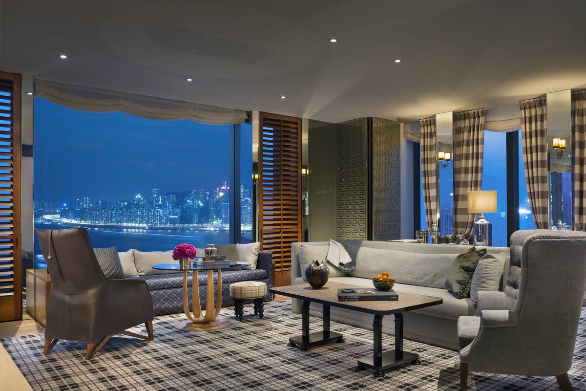 A modern living room with a city view, a sofa, armchairs, a coffee table, and a decorative vase.