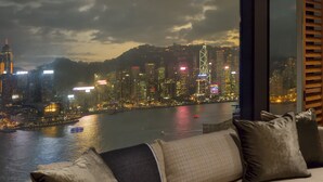 A living room with a sofa, a coffee table, and a view of a cityscape at night. - Rosewood Hong Kong (Kowloon)