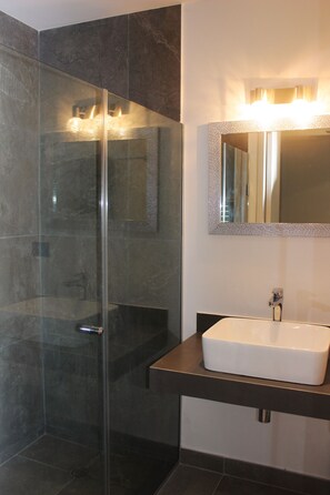 A modern bathroom with a glass-enclosed shower, a white sink, and a mirror with a textured frame.