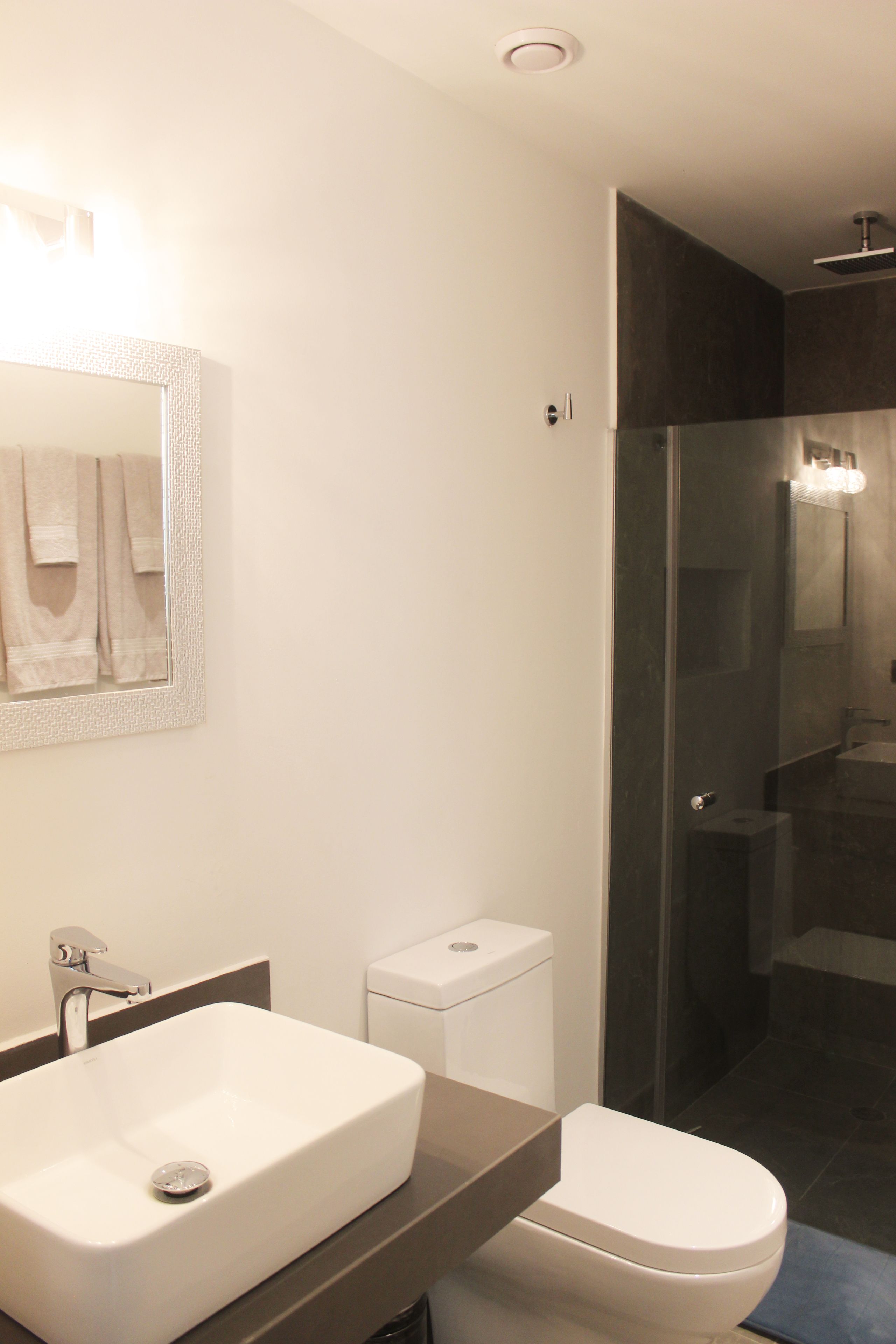 A modern bathroom with a large white sink, a toilet, and a glass-enclosed shower area.