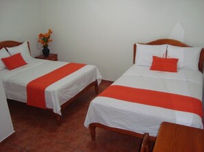 Two single beds with white and red bedding, a wooden nightstand with a vase of flowers, and a wooden chair.
