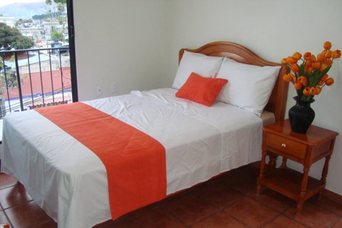A neatly made bed with a white and orange bedspread, a wooden headboard, and a nightstand with a vase of flowers.