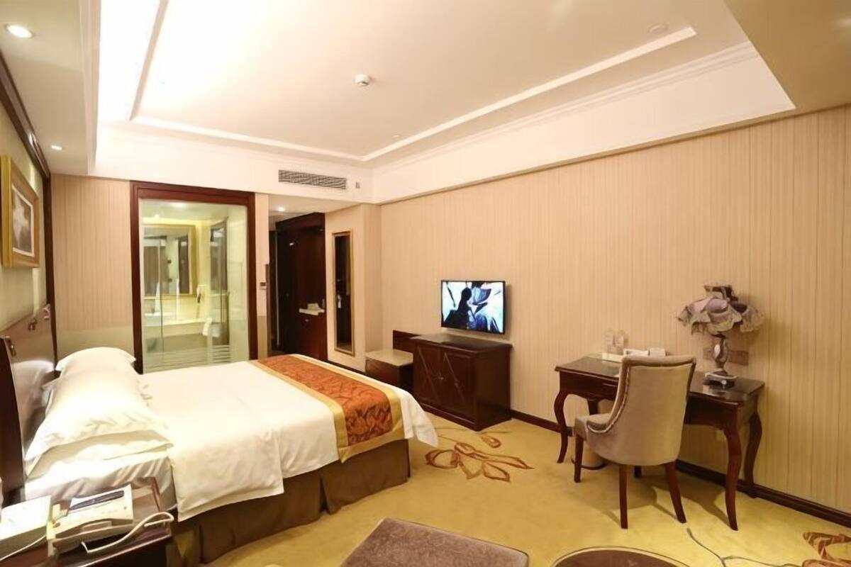 Ett hotellrum med en säng, ett skrivbord, en stol, en tv och en spegel.