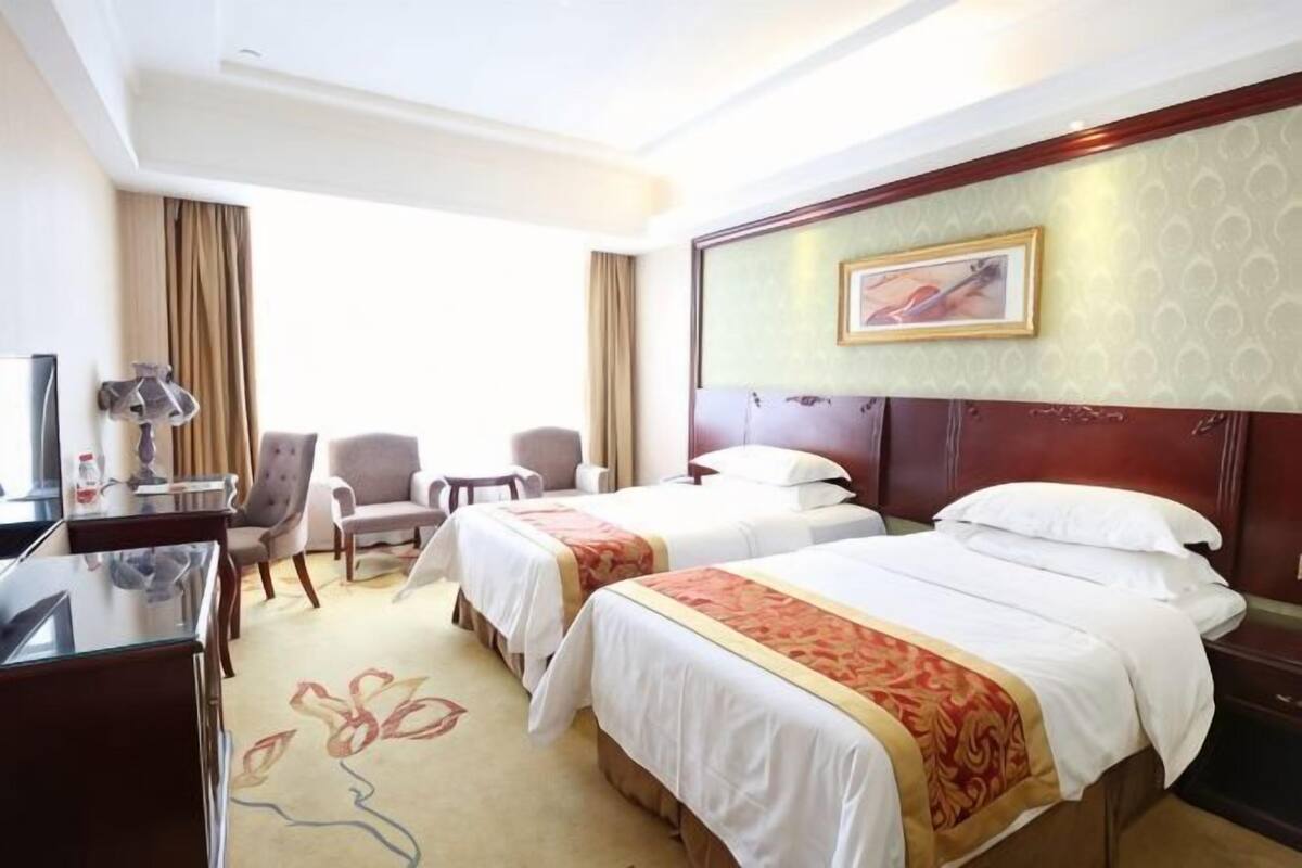Ett hotellrum med två sängar, ett skrivbord, en stol, en TV och ett fönster.