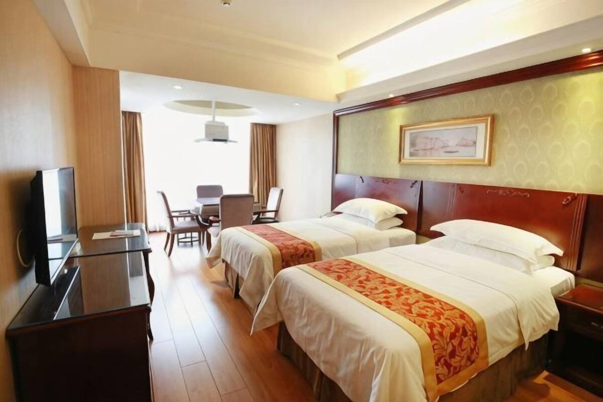 Ett hotellrum med två sängar, ett skrivbord, en stol, en TV och ett stort fönster.