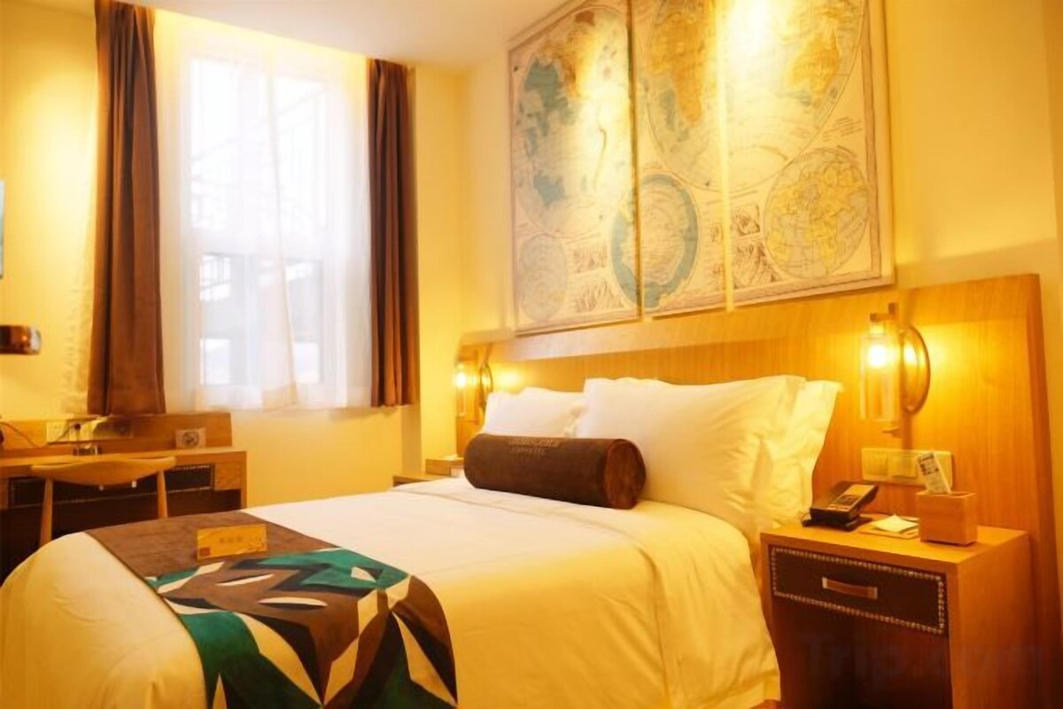 A hotel room with a bed, bedside table, lamp, and a large map on the wall.