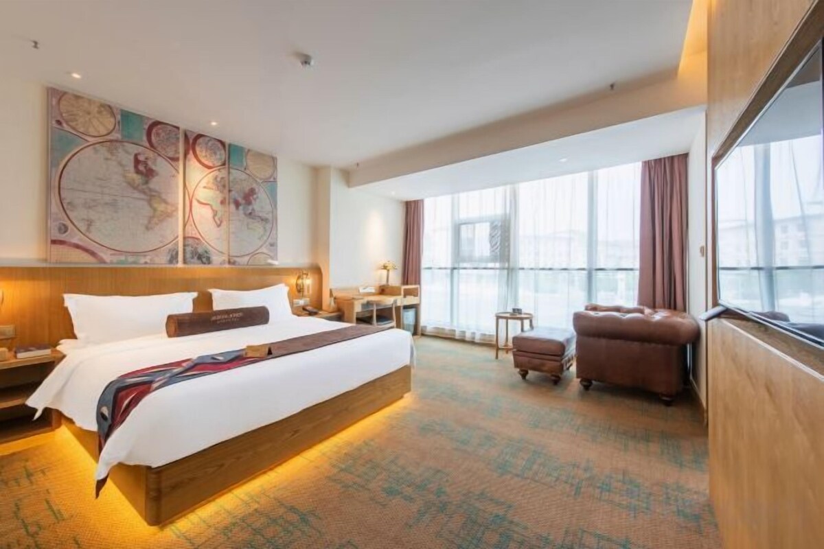A hotel room with a large bed, a desk, a chair, and a window with curtains.