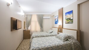 Et hotelværelse med to senge, et fladskærms-tv, en aircondition og to billeder i rammer på væggen.
