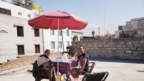 Two people seated at an outdoor table with a red umbrella, a striped tablecloth, and a stone wall in the background. - Casona de Sillar (Arequipa)