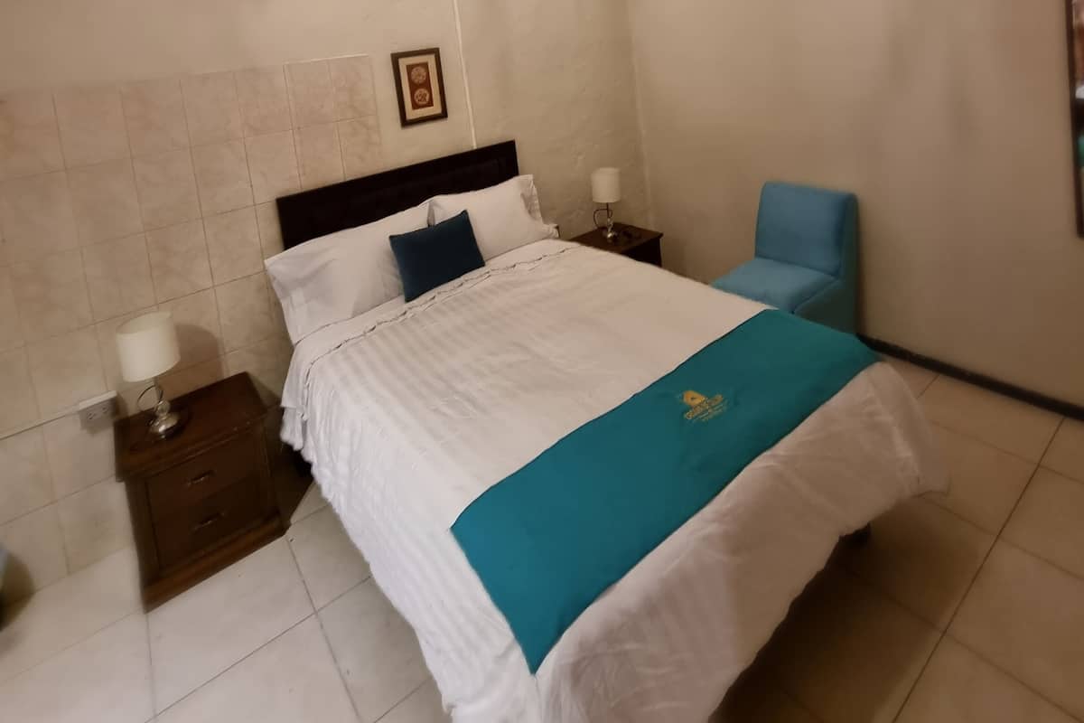 A hotel room with a bed, a nightstand, a chair, a chandelier, and a wall with a picture.