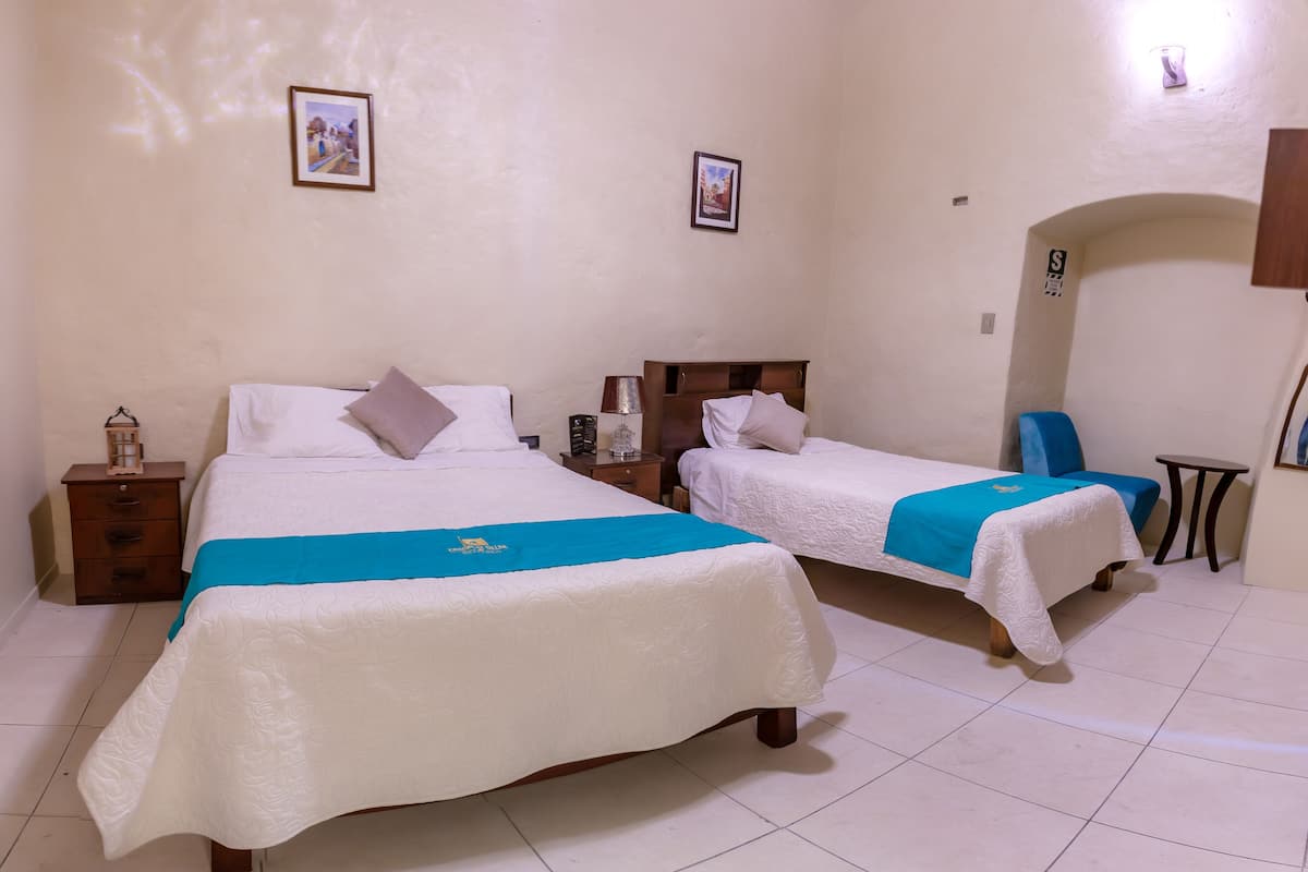 Two single beds with white bedding and blue headboards, a small bedside table with a lamp, and a framed picture on the wall.