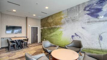 A modern hotel room with a large wall mural, a flat-screen TV, a round table, and a seating area with chairs.