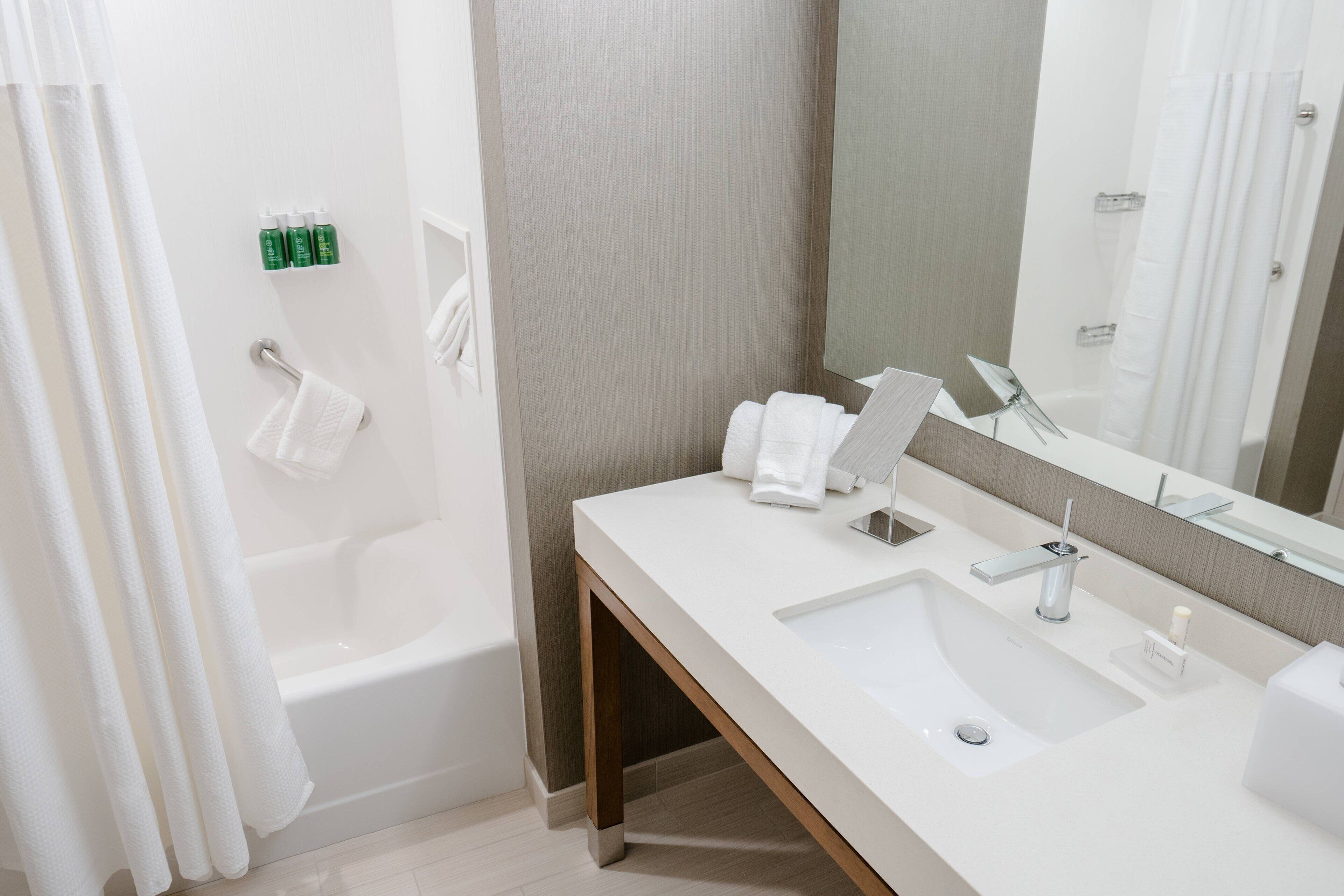 A modern bathroom with a bathtub, a large mirror, and a white sink.