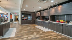 Una cocina moderna con armarios de madera oscura, piso con patrón de espiga y una isla central con un tazón rojo de fruta.