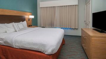 Quarto de hotel com uma cama grande, cabeceira de madeira, mesa de cabeceira com abajur, televisão e guarda-roupa.