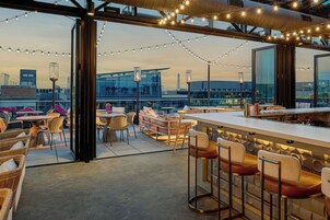 An outdoor seating area with tables and chairs, string lights, and a view of the cityscape.