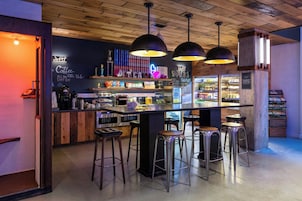 A bar area with wooden ceiling, pendant lights, stools, shelves with snacks and drinks, and a neon sign.