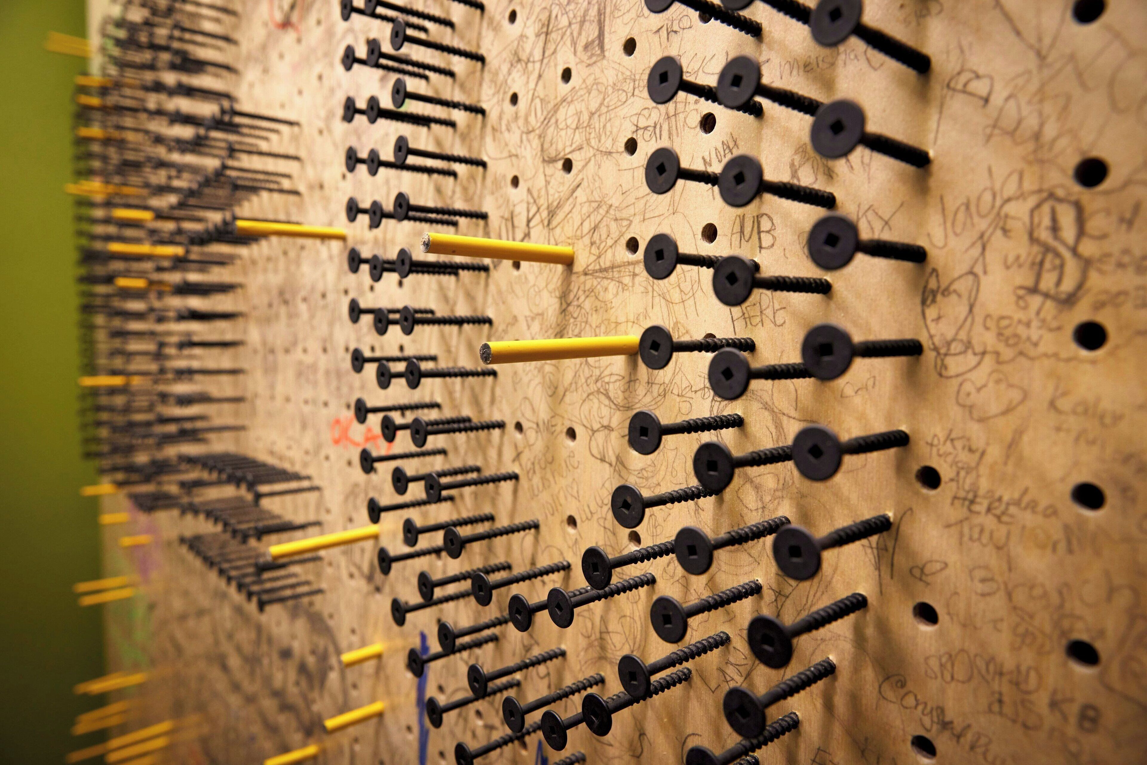 A wall with numerous black and yellow screws arranged in rows.