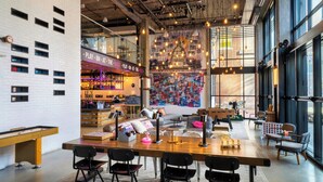 A spacious indoor area with a long wooden table, several chairs, a sofa, and a bar area with shelves and bottles. - Moxy Washington DC Downtown (Washington)