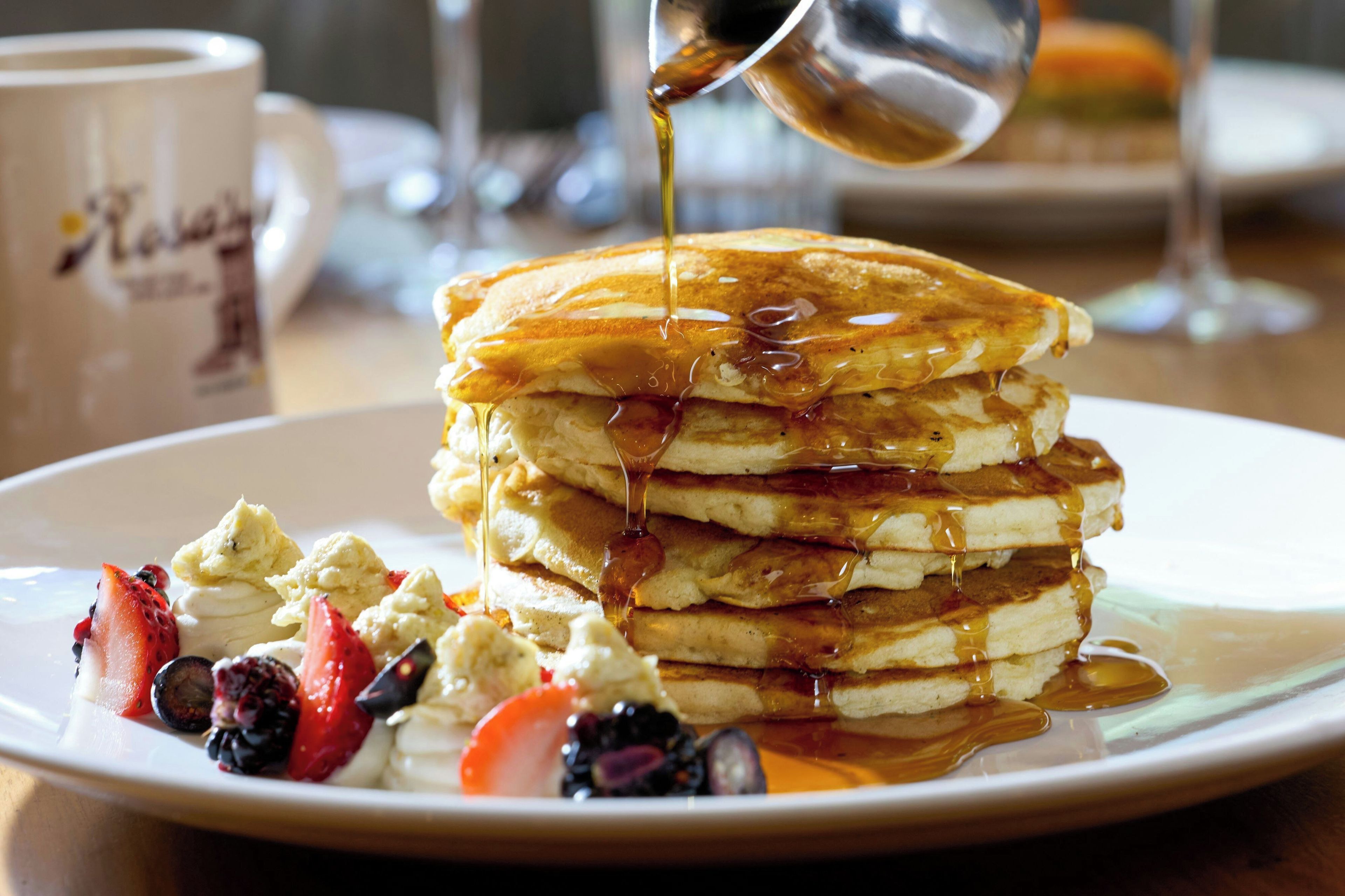 A stack of pancakes with syrup and fruit on a plate.