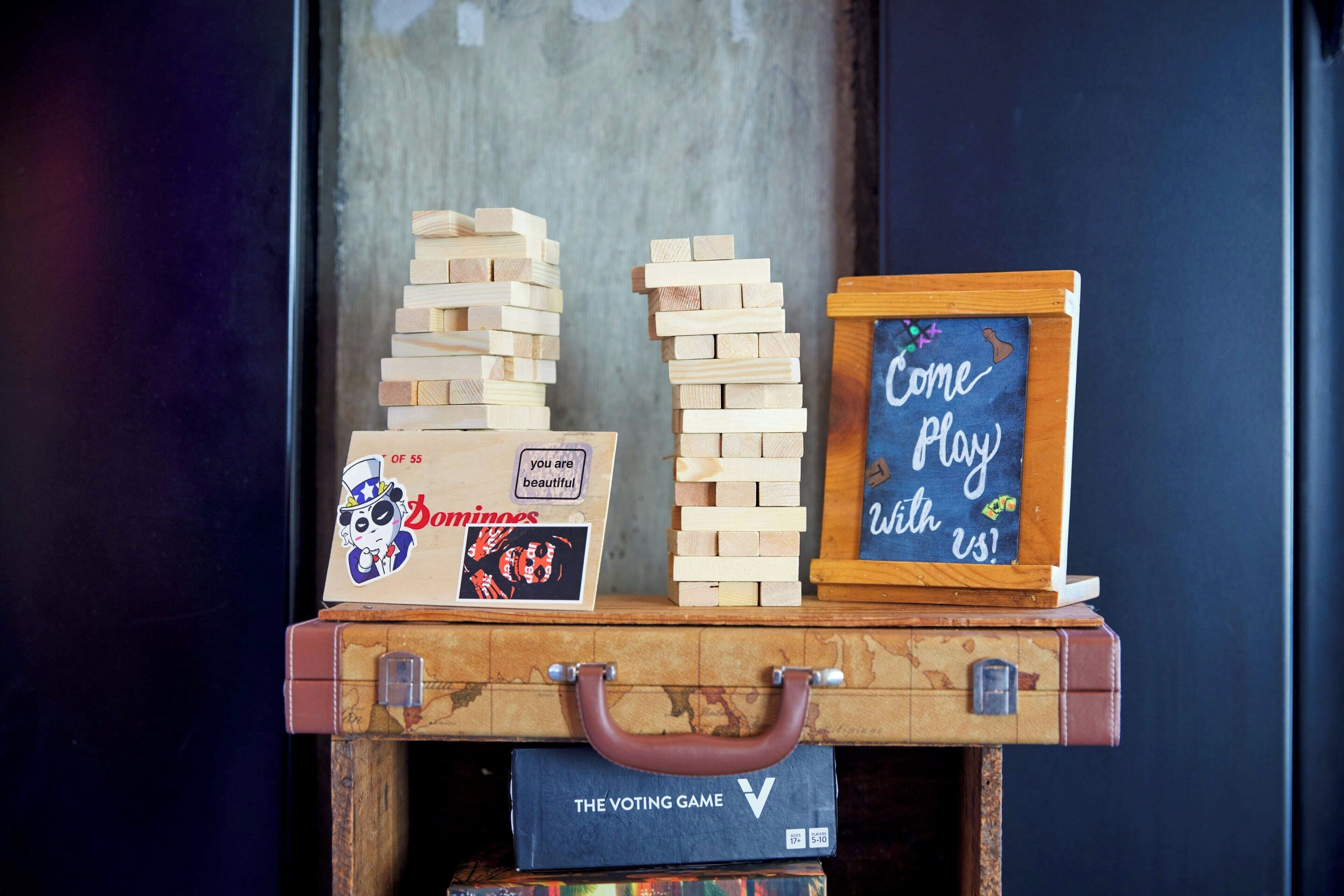 A wooden suitcase with a handle, stacked dice, a Dominoes box, and a chalkboard sign.