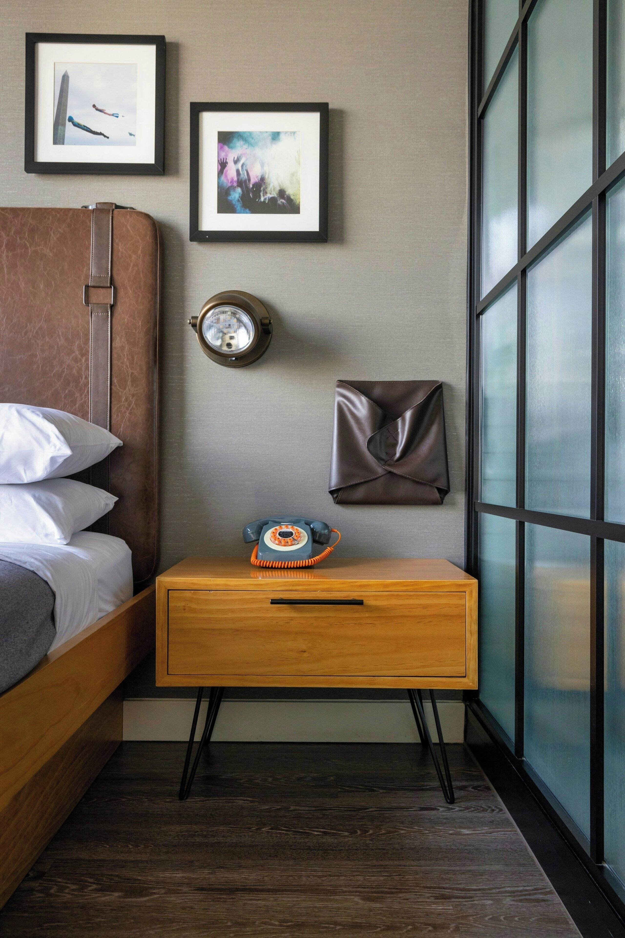 A bedroom with a bed, a wooden nightstand, a clock, and framed pictures on the wall.