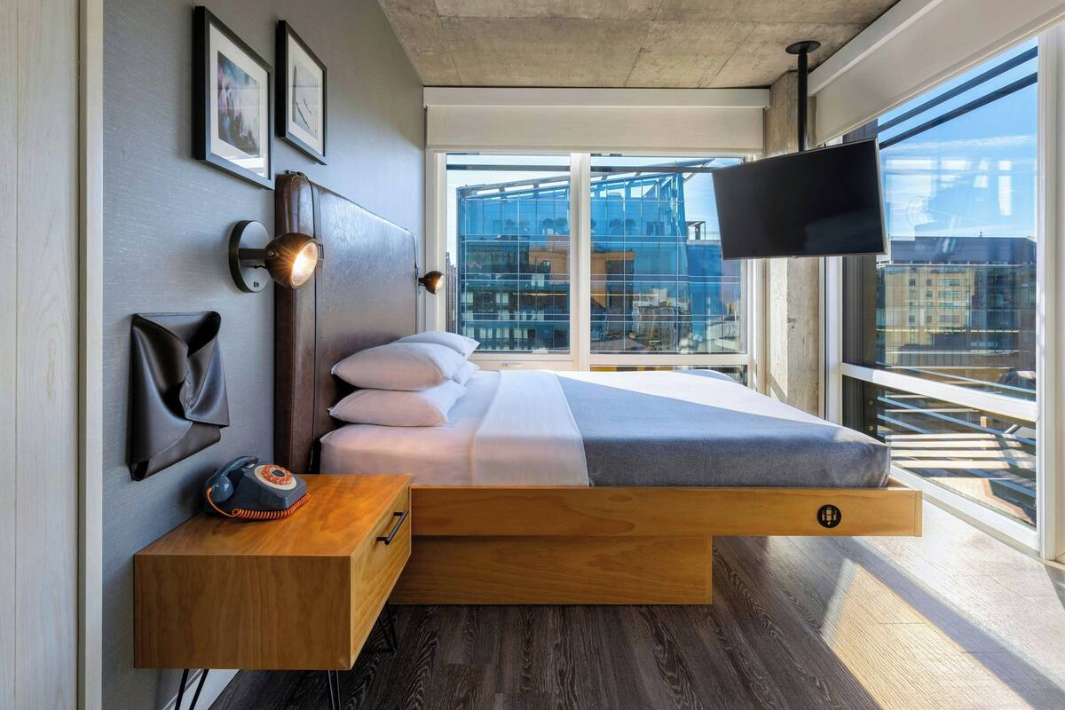 A modern bedroom with a bed, bedside table, lamp, and a TV mounted on the wall.