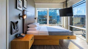 Quarto moderno com cama, mesa de cabeceira, luminária e televisão na parede.