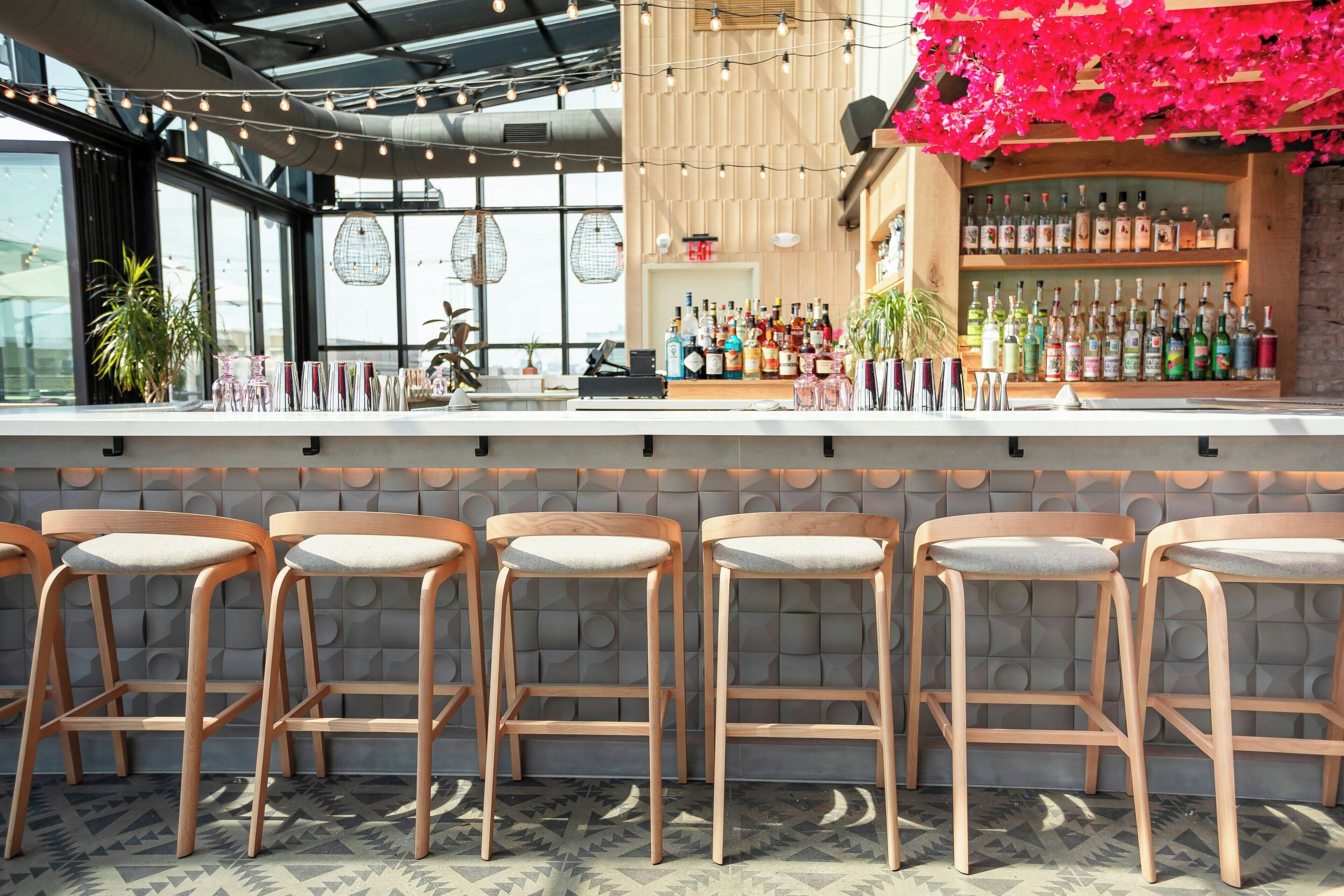A bar area with wooden stools, a bar counter, and a variety of bottles.