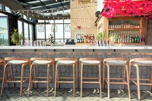 A bar area with wooden stools, a bar counter, and a variety of bottles.