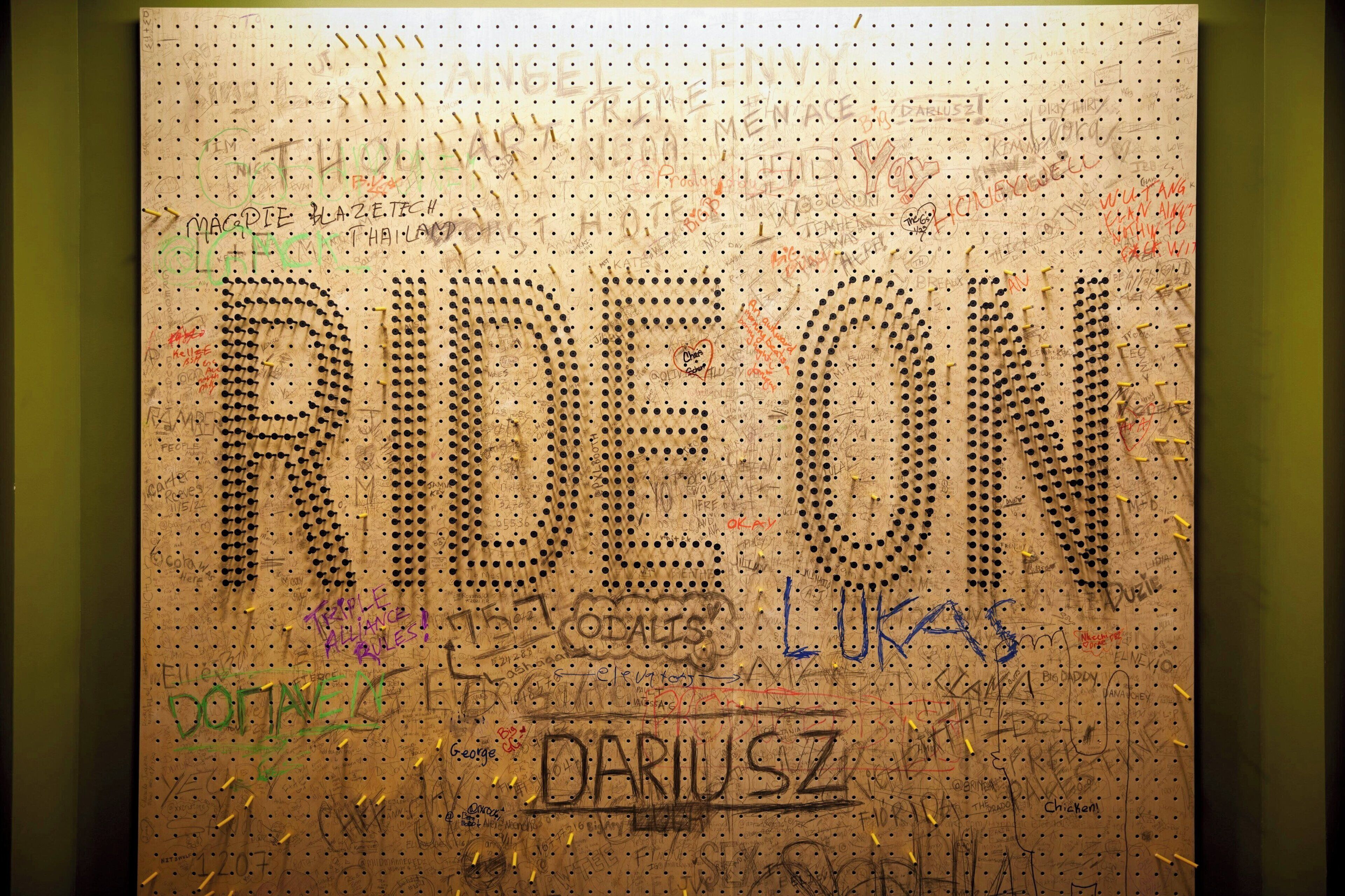 Een muur met verschillende teksten en tekeningen, waaronder het woord "RIDE ON" en namen zoals "DARIUSZ" en "LUKAS".