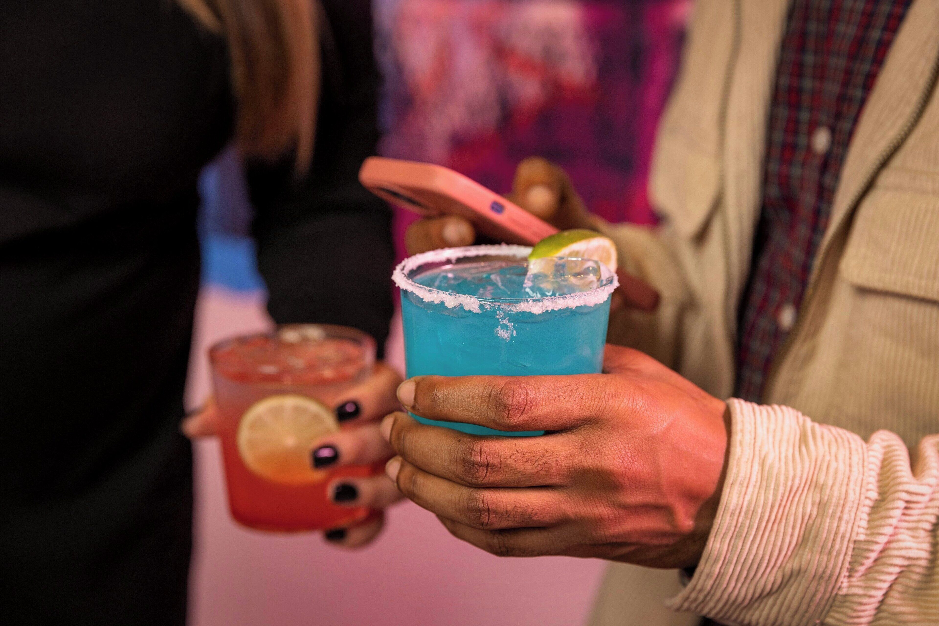 A person holding a blue cocktail with a lime garnish.