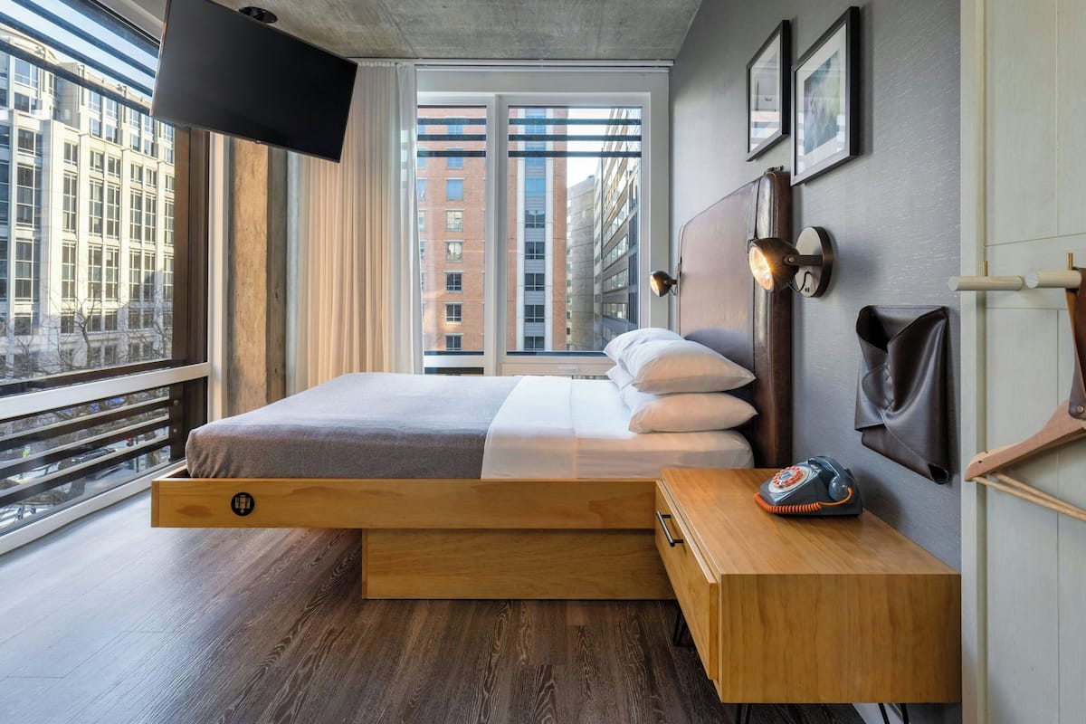 A modern bedroom with a bed, wooden nightstand, and a telephone.