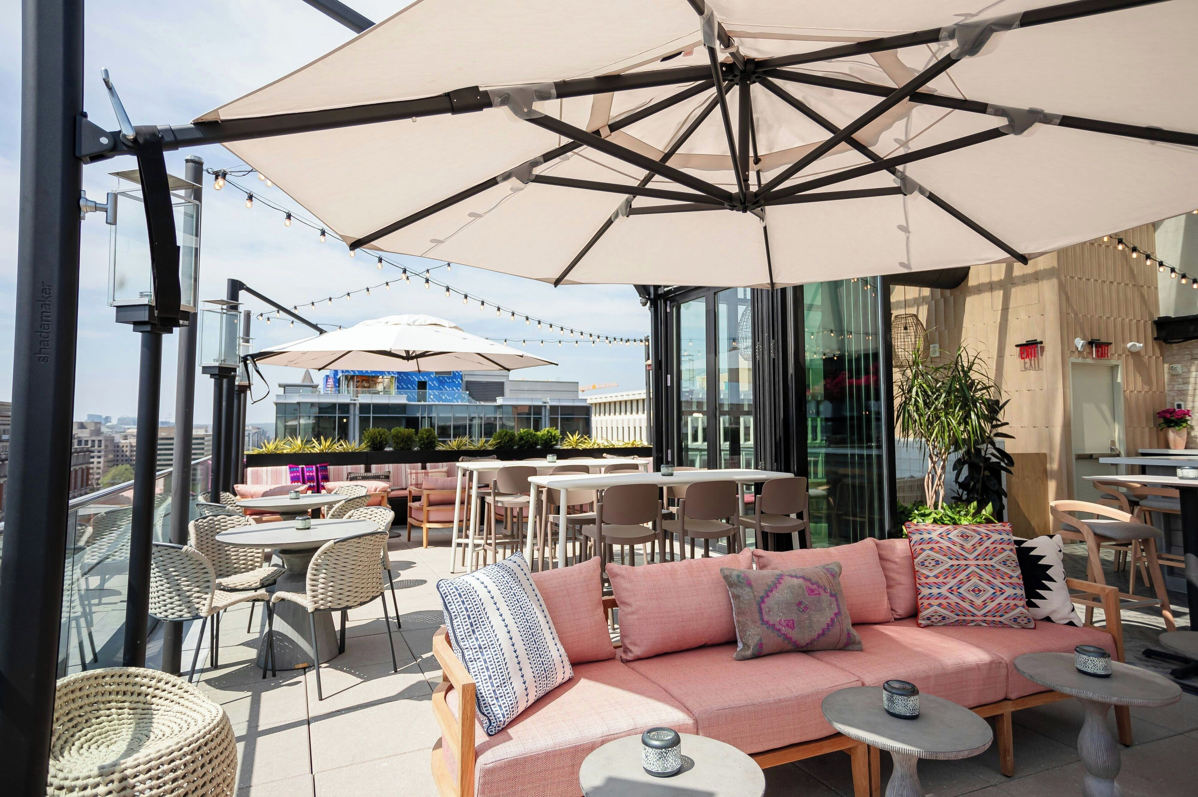 An outdoor seating area with a sofa, chairs, and tables under large umbrellas, overlooking a cityscape.