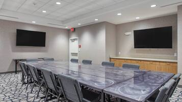 Uma sala de conferências com uma mesa comprida, cadeiras, uma TV de tela plana, um quadro branco e uma pequena área de copa.