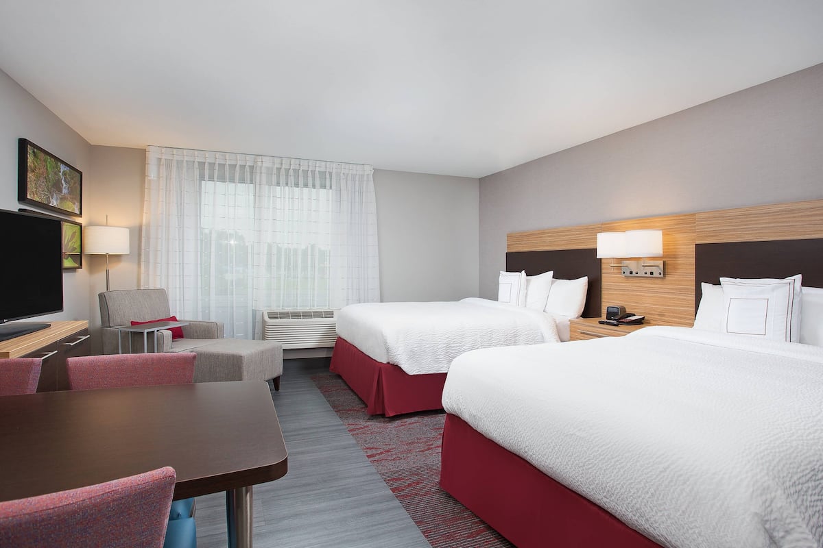 A hotel room with two beds, a desk, a chair, a TV, and a window with curtains.
