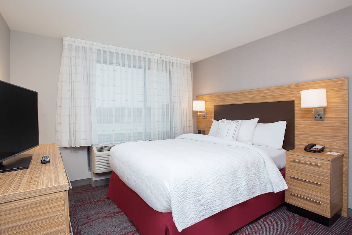 A hotel room with a large bed, a TV, a bedside table, and a lamp.