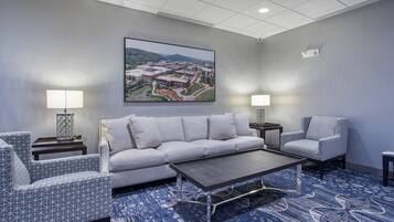 A modern hotel room with a gray sofa, patterned armchairs, a coffee table, and a large landscape painting on the wall.